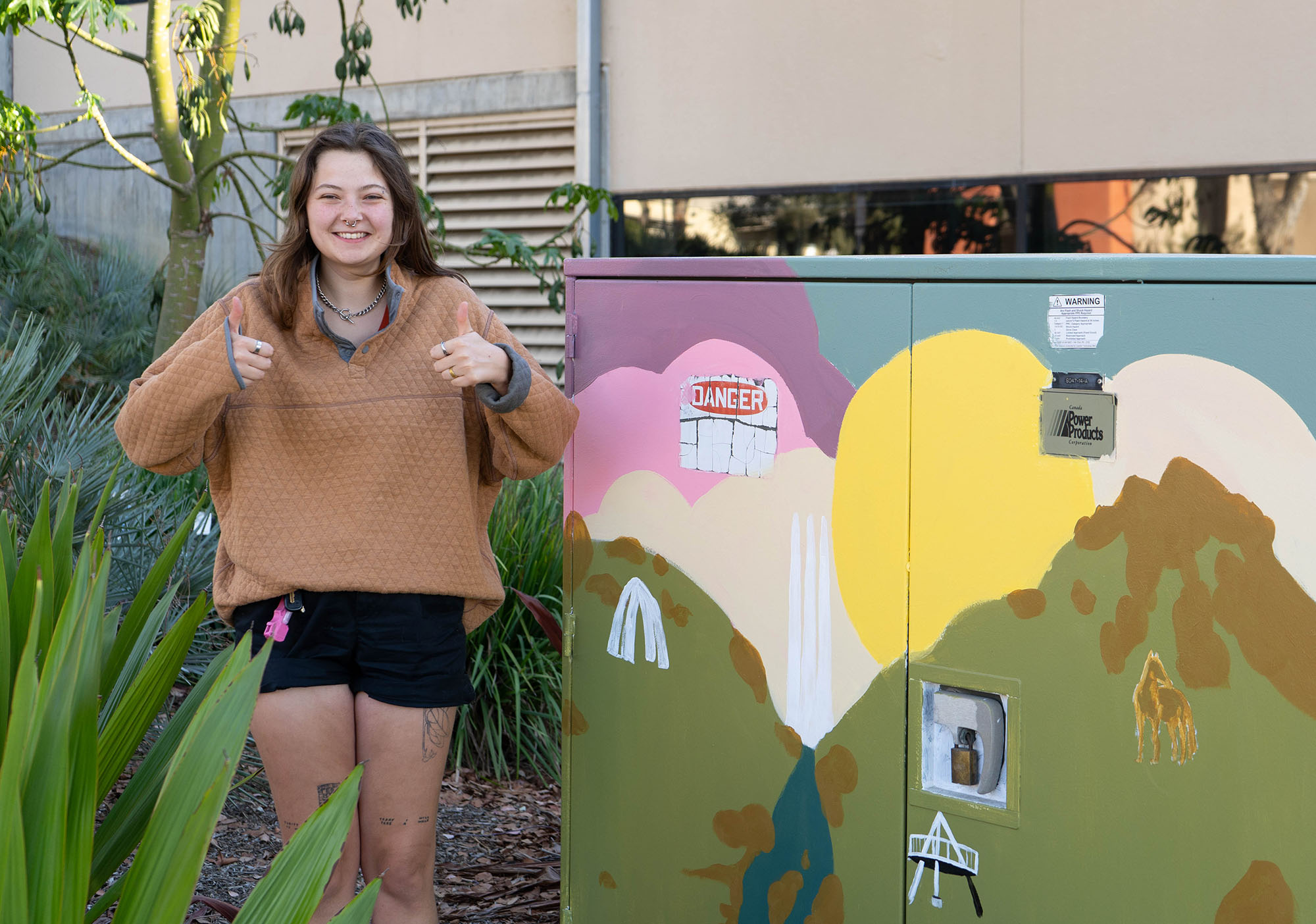 Girl give two thumbs up, standing next to the utility box