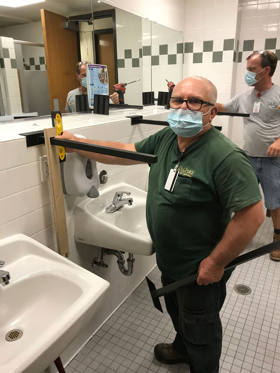 Carpenters are posing for the picture with plexiglass barrier material in the restroom.