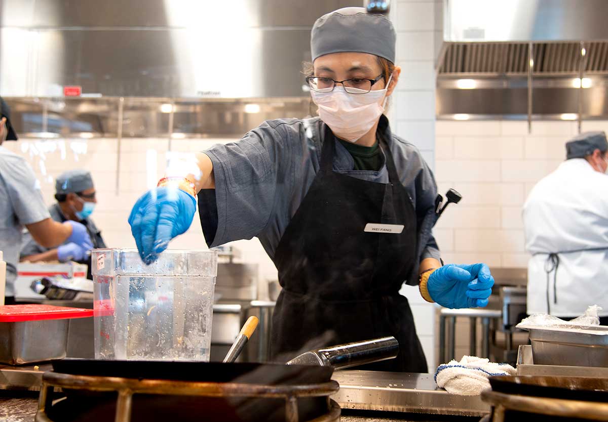 Cal Poly employee in one of the campus kitchens wearing a mask and preparing food